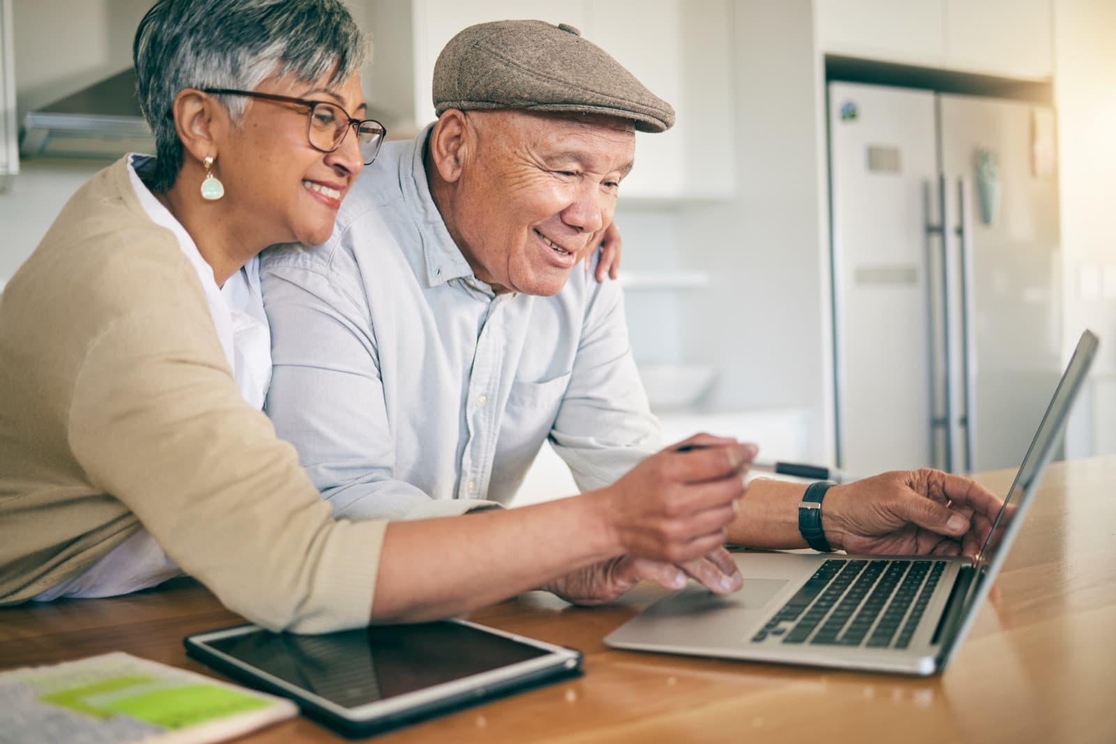 A cheerful older couple looking at a laptop together at their kitchen table